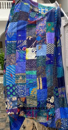 a large blue quilt is hanging on a clothes line outside an apartment building with a cat in the foreground