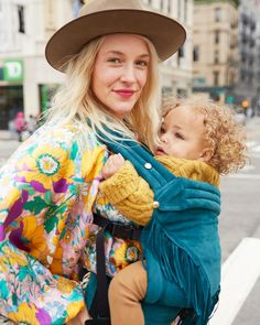 a woman in a hat holding a baby wearing a blue and yellow blanket on her back