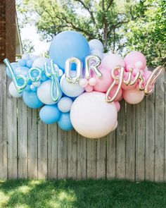 balloons that spell out the word baby girl hanging from a wooden fence in front of a yard