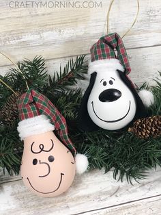 some ornaments are hanging on a white wooden wall with pine cones and evergreen branches in the foreground