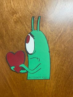 a green alien holding a heart on top of a wooden table with the word anthan z2