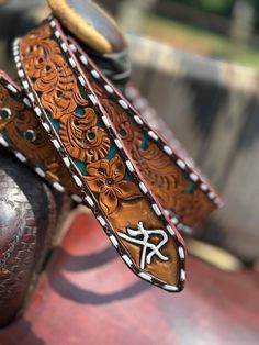 a pair of brown and white leather belts on top of a red chair with an ornate design