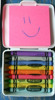 a pink box filled with crayons and a smiley face drawn on it