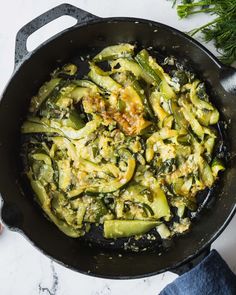 a skillet filled with green vegetables on top of a white counter next to some herbs