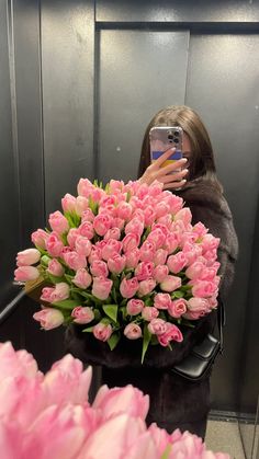 a woman taking a selfie while holding a bouquet of pink tulips