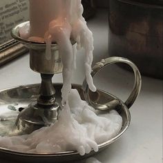 a candle that is on top of a silver plate with water pouring out of it