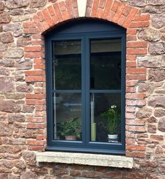 a brick wall with two windows and potted plants in the window sill below