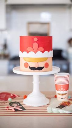 there is a cake with a mustache on it and cups next to the cake stand