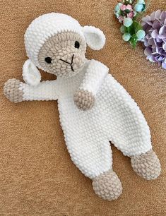 a knitted teddy bear laying on the ground next to some purple and white flowers