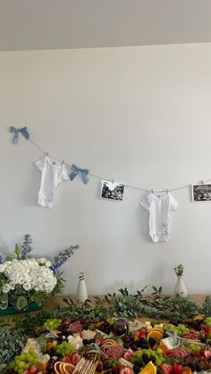 an arrangement of fruits and vegetables on a table with baby ones hanging from the clothes line