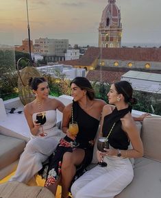 three beautiful women sitting on top of a couch drinking wine and having drinks in front of the camera