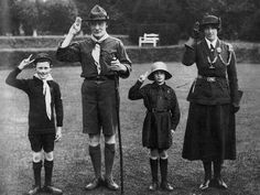 an old black and white photo shows three children in uniforms standing on grass with their hands up