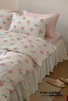 a white bed with pink and green flowers on the comforter is next to a pair of slippers