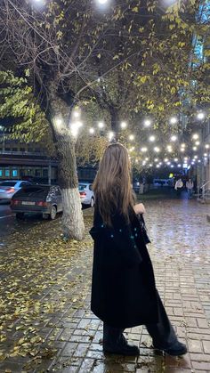 a woman sitting on the ground in front of a tree with lights hanging from it