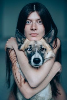 a woman is holding a dog with her arms around her neck and looking at the camera