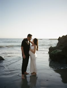 a man and woman standing on the beach next to each other with their arms around each other