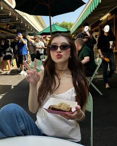 a woman sitting at an outdoor table holding a piece of cake in front of her