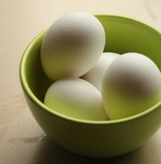 four eggs in a green bowl on a table