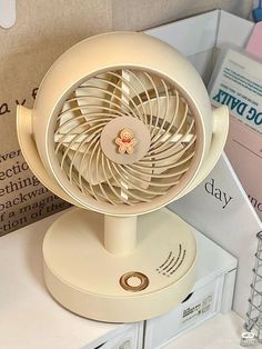 a white table top fan sitting on top of a stack of books and papers next to a pile of folders