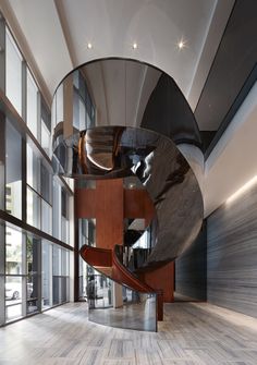 a spiral staircase in an office building with glass walls and wood flooring on both sides