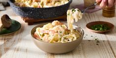 a person is eating pasta with shrimp and parsley in a bowl on a table