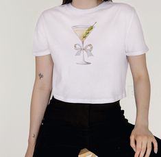 This Martini Baby Tee is for the girls! Whether you're sipping martinis at a rooftop bar or simply enjoying a cozy night in, this tee is the perfect choice for the girls who love to embrace their feminine side with flair. It has that effortlessly stylish fit with raw-edge sleeves and hems and a cropped, relaxed fit.  .: 65% polyester, 35% combed, ring-spun cotton .: Extra light fabric  .: Raw sleeve and bottom hems HOW TO ORDER:  SELECT YOUR SIZE FROM THE DROP DOWN AND THEN "Add to Cart" PLEASE SIZE UP 1-2 SIZES FOR A MORE 'OVERSIZED' LOOK CARE/ WASH .: Machine wash: warm (max 40C or 105F); Non-chlorine: bleach as needed; Tumble dry: medium heat; Iron, steam or dry: low heat; Do not dry clean! PLEASE ALLOW 3-7 BUSINESS DAYS FOR PRODUCTION.  Please be careful to check your address and size Cute Fitted T-shirt For Party, Cute Short Sleeve Party Tops, Cute Fitted Party T-shirt, Cute Cotton Party Tops, Cotton Short Sleeve T-shirt For Party, Fitted Cotton T-shirt For Party, White Cotton T-shirt For Party, Party Cotton Top With Short Sleeves, Short Sleeve Cotton Party Top