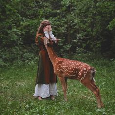 a woman standing in the grass next to a deer with it's head on her hand