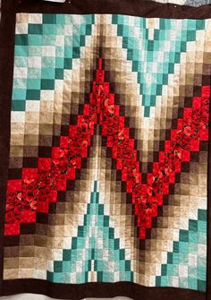 a quilt with red flowers on it sitting on top of a white tablecloth next to a wall