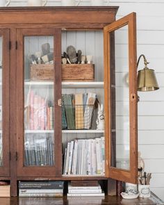 a wooden cabinet with glass doors and shelves filled with books, magazines and other items