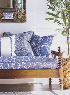 a couch with blue and white pillows in front of a mirror on the wall above it