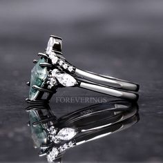 a close up view of an engagement ring with green and white stones on it's sides