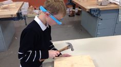 a young boy is working on woodworking with a hammer and visor over his head