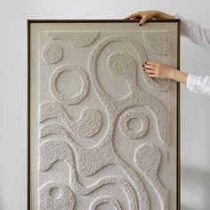 a woman is holding up a large art piece with white paint and swirls on it