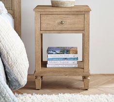 a wooden night stand with two books on it and a basket sitting on top of one