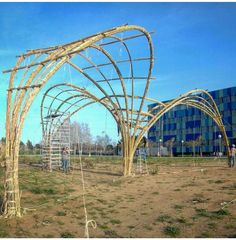 an arch made out of branches in the middle of a field with people working on it