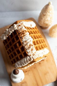 a wooden cutting board topped with a waffle covered in icing and whipped cream