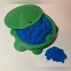 a blue substance in a green container next to it's lid on a white surface