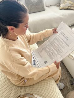 a woman sitting on a couch reading a paper