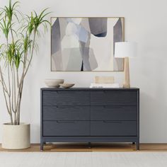 a black dresser sitting next to a potted plant and a painting on the wall