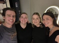 a group of people standing next to each other in front of a mirror smiling at the camera