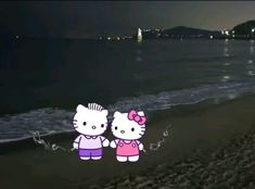 two hello kitty stickers sitting on top of a beach next to the ocean at night