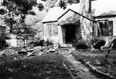 black and white photo of an old house with junk piled on the front lawn in front of it