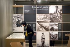 a woman standing in front of a wall with pictures on it and people looking at them