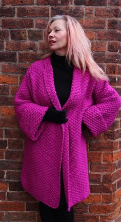 a woman standing next to a brick wall wearing a bright pink coat and black gloves