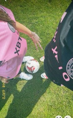 a woman in pink shirt touching soccer ball on grass