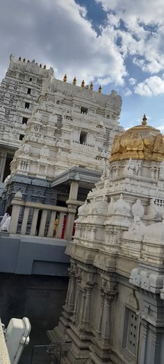 an ornate white and gold building with statues on the sides, against a cloudy blue sky