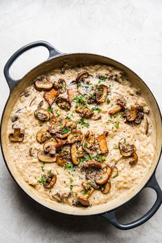 a pan filled with rice and mushrooms on top of a white countertop next to a spoon