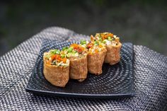 small appetizers are arranged on a black plate, ready to be eaten at an outdoor event