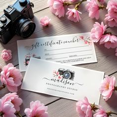 two business cards sitting on top of pink flowers next to a camera and a lens