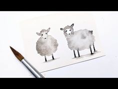 two sheep standing next to each other on top of a white surface with a paintbrush